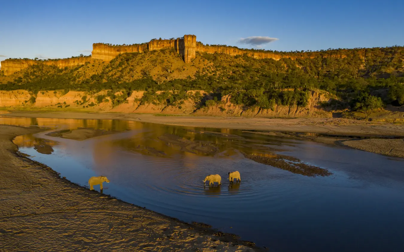 Elephants drinking from river below dramatic cliff formations at sunset, Chilo Gorge Safari Lodge, Gonarezhou & Malilangwe, Zimbabwe