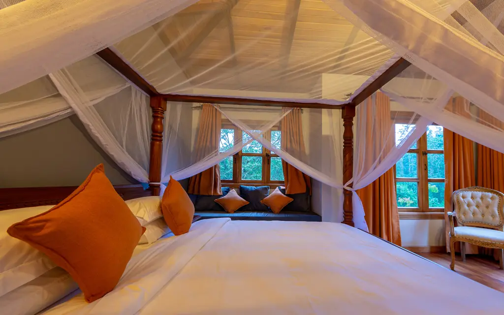 Luxurious four-poster bed with sheer canopy and orange accents, Chimpundu Lodge, Kibale Forest, Uganda