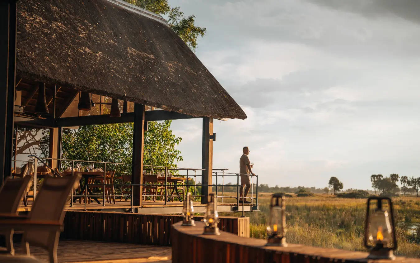 Guest standing on wooden deck overlooking savanna landscape, Chitabe Camp, The Okavango Delta, Botswana