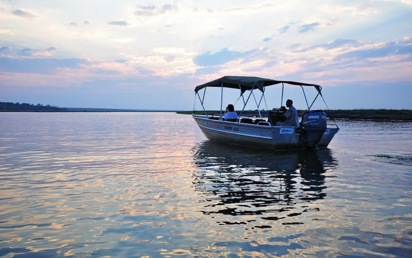 Motorboat with passengers on calm water at sunset, Chobe Chilwero, Chobe, Botswana