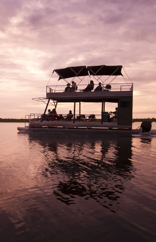 Two-deck houseboat with guests on calm waterway at sunset, Chobe, Botswana