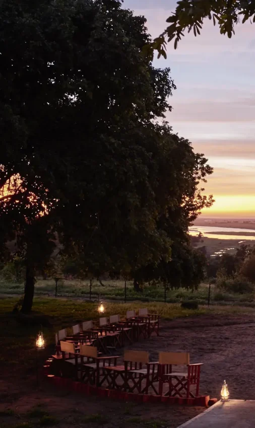 Outdoor amphitheater seating arranged around fire pit overlooking river at dusk, Chobe Chilwero, Chobe, Botswana