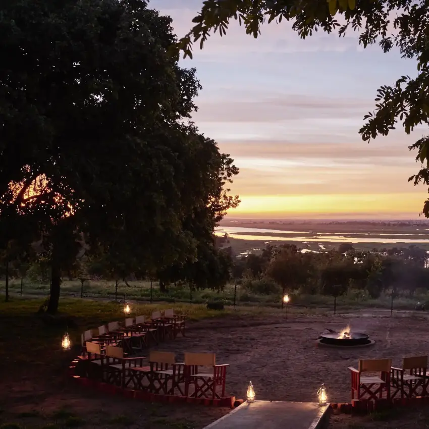 Outdoor amphitheater seating arranged around fire pit overlooking river at dusk, Chobe Chilwero, Chobe, Botswana