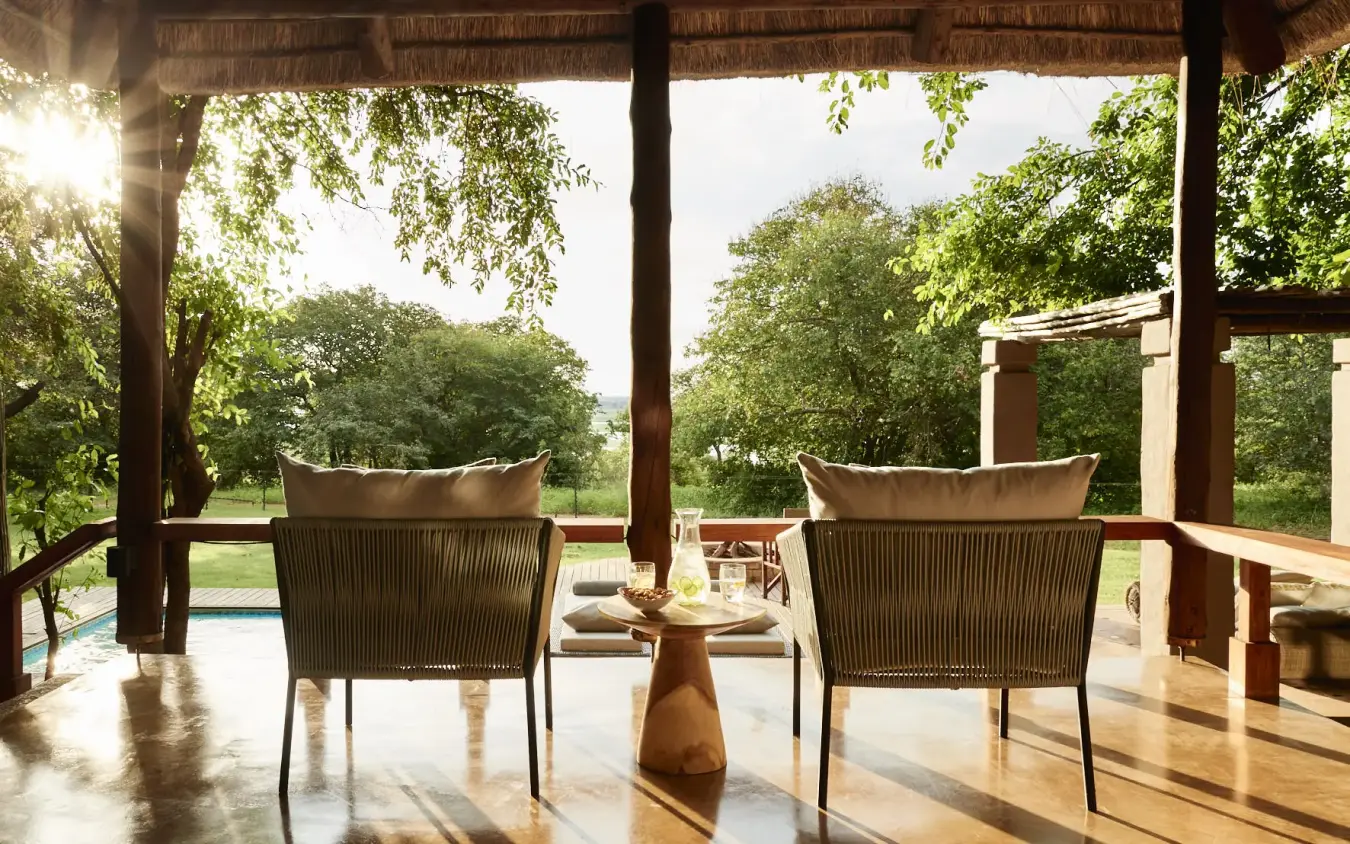 Lounge chairs on covered terrace overlooking pool and woodland landscape, Chobe Chilwero, Chobe, Botswana