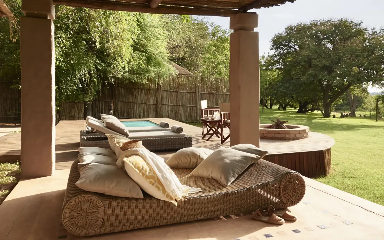 Wicker daybed with cushions on wooden deck overlooking manicured gardens, Chobe Chilwero, Chobe, Botswana