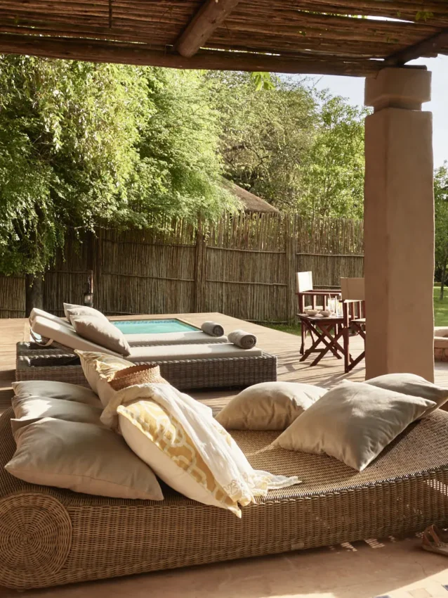 Wicker daybed with cushions on wooden deck overlooking manicured gardens, Chobe Chilwero, Chobe, Botswana