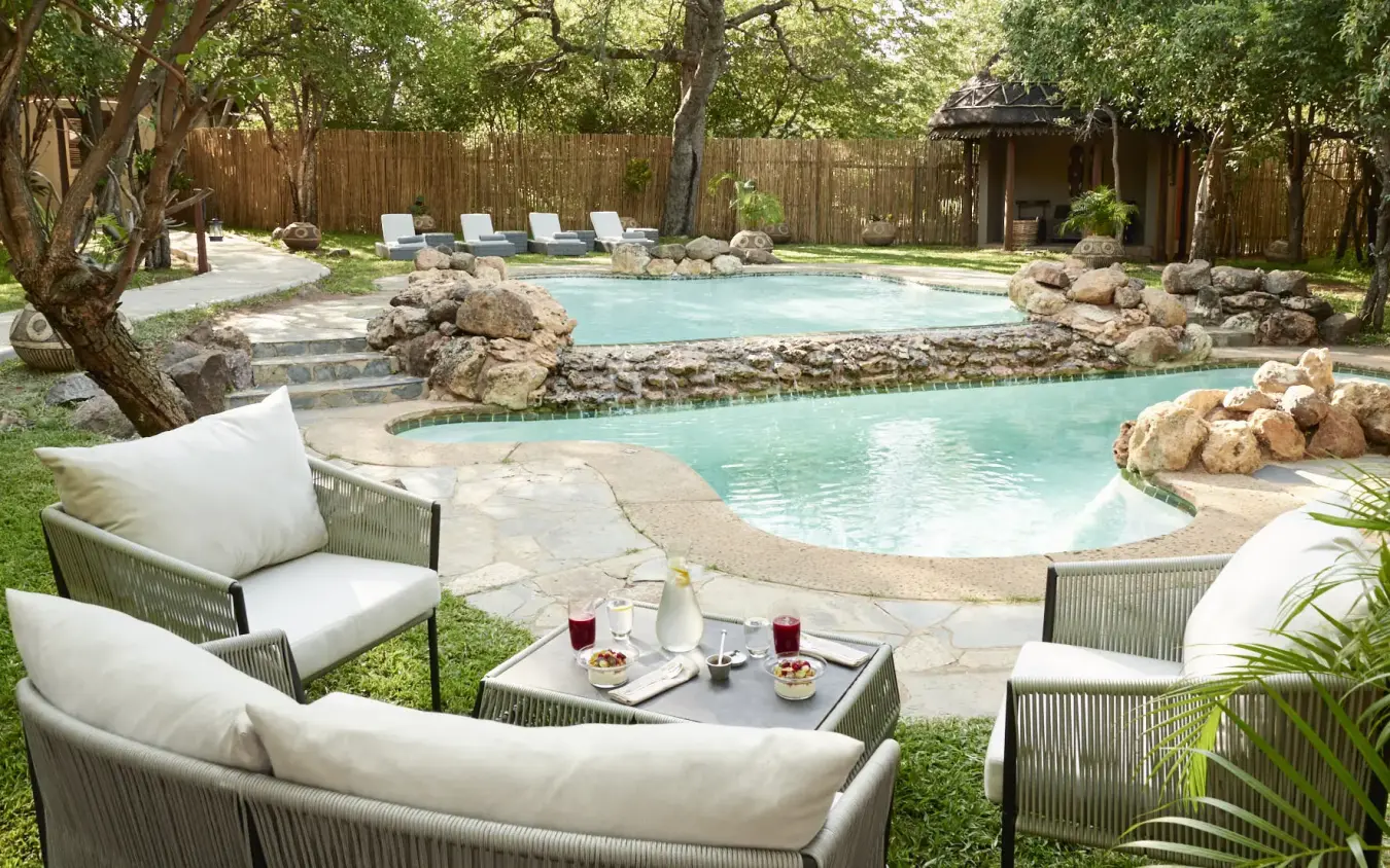 Luxury pool resort with lounging areas nestled among trees and natural rock features, Chobe Chilwero, Chobe, Botswana