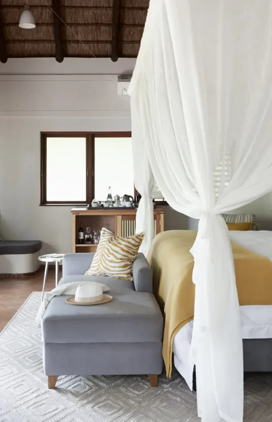 Canopied bed with white drapes in light-filled bedroom suite, Chobe Chilwero, Chobe, Botswana