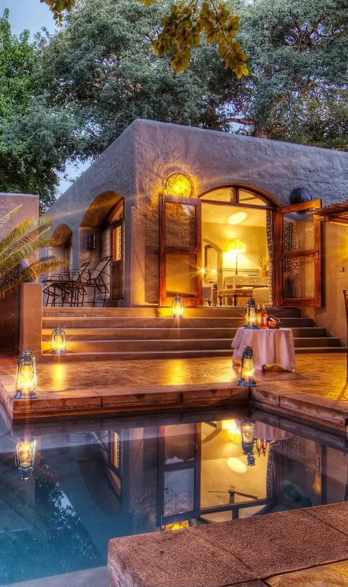 Illuminated lodge with pool reflecting evening lights and surrounding vegetation, Chobe Game Lodge, Chobe, Botswana
