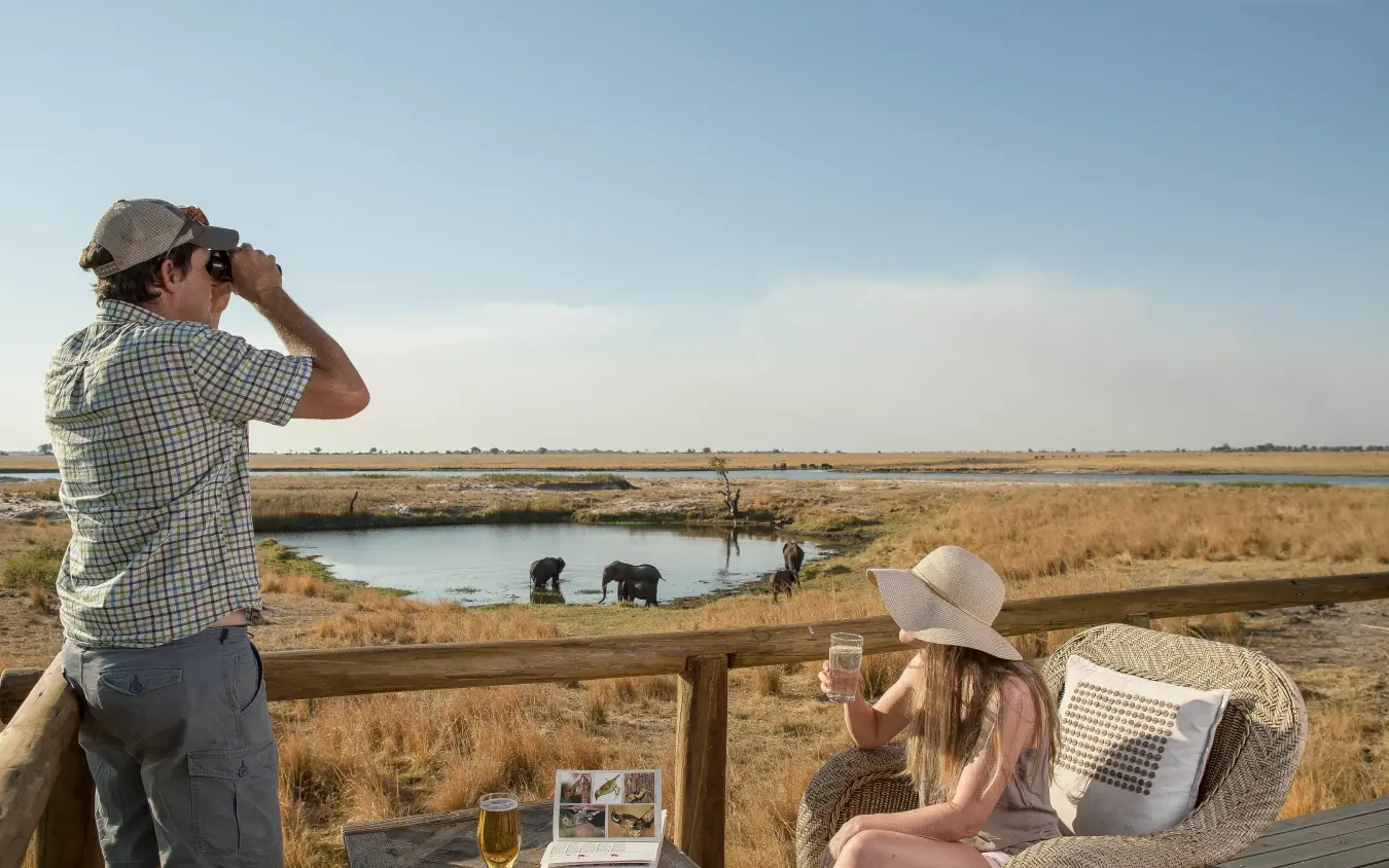 Guests viewing wildlife from observation deck at waterhole, Chobe Savanna Lodge, Zambezi Region, Namibia