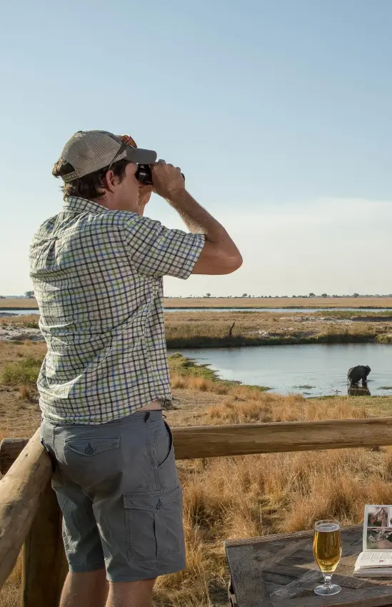 Guests viewing wildlife from observation deck at waterhole, Chobe Savanna Lodge, Zambezi Region, Namibia