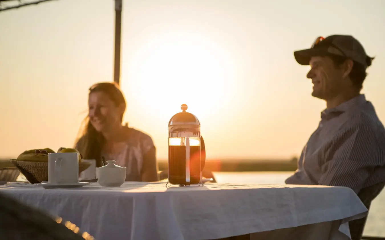 Guests dining at sunset table overlooking water, Chobe Savanna Lodge, Zambezi Region, Namibia