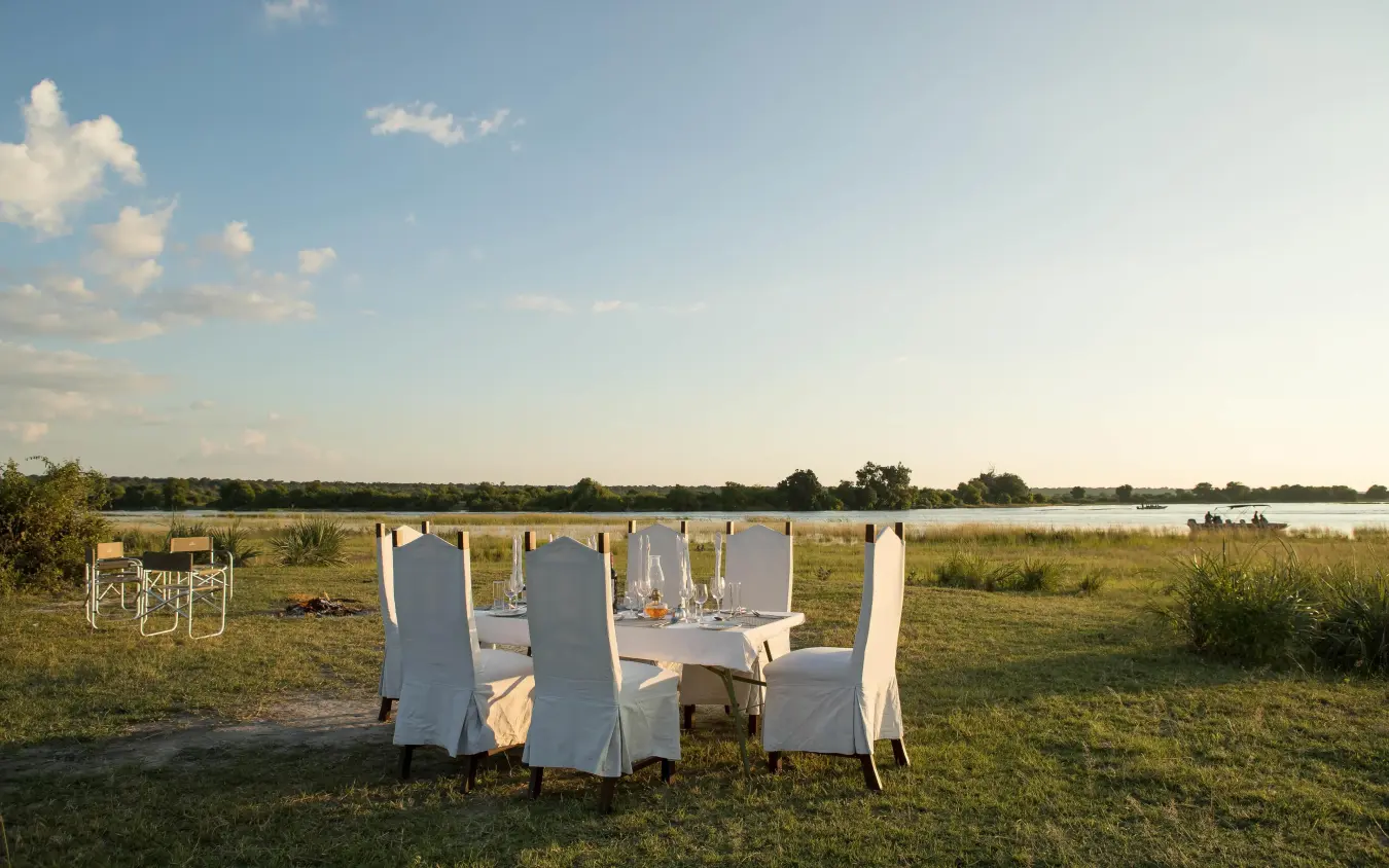 Outdoor dining setup on savanna overlooking waterhole, Chobe Savanna Lodge, Zambezi Region, Namibia