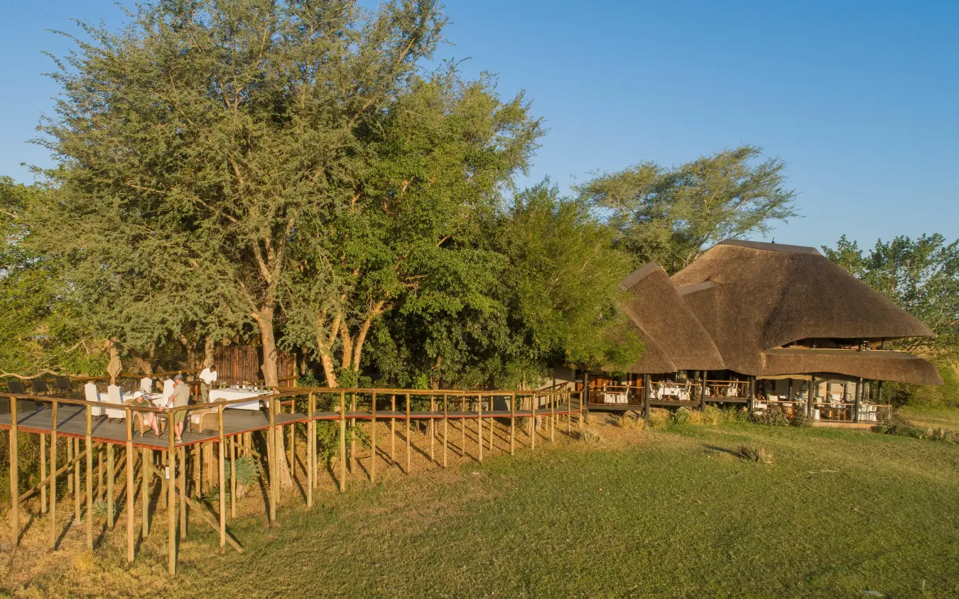 Thatched-roof lodge buildings with wooden deck and large trees, Chobe Savanna Lodge, Zambezi Region, Namibia