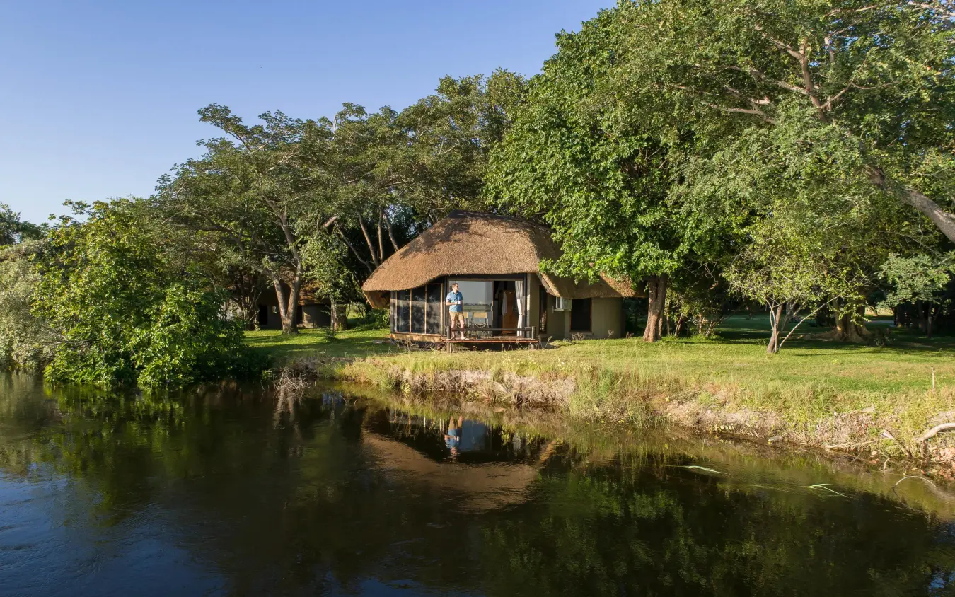 Thatched roof lodge beside river with mature trees, Chobe Savanna Lodge, Zambezi Region, Namibia