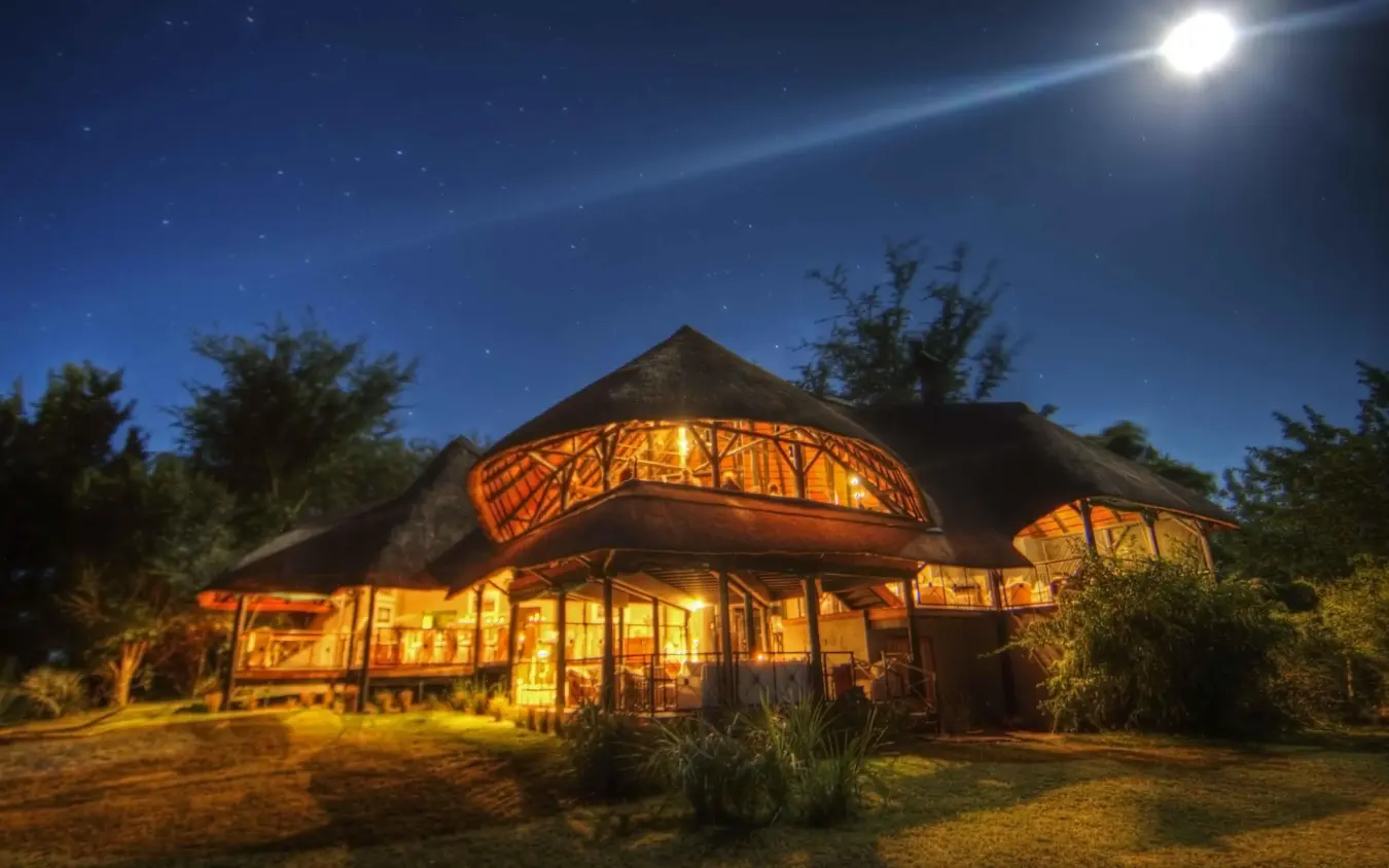 Illuminated thatched-roof lodge building under moonlight at night, Chobe Savanna Lodge, Zambezi Region, Namibia