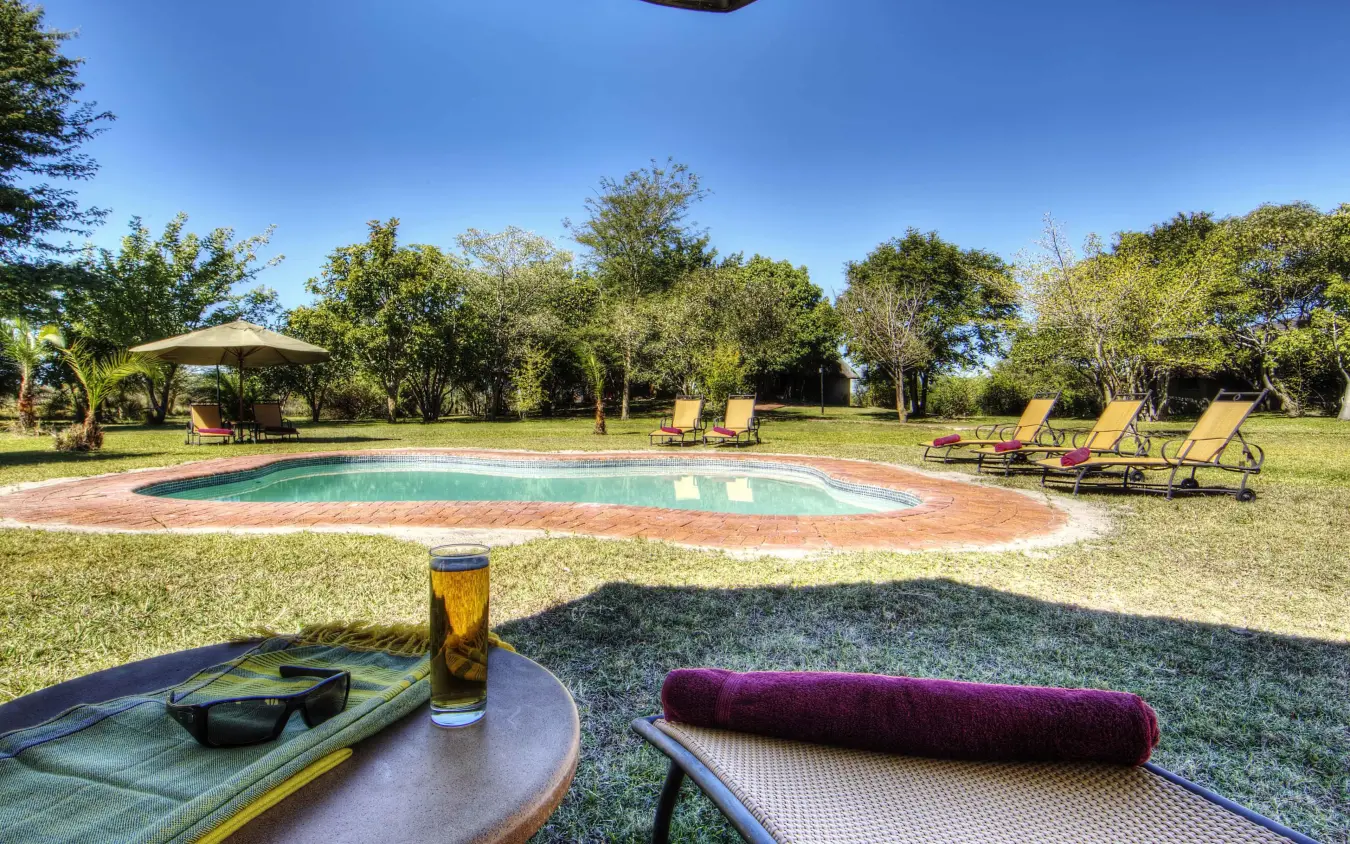 Resort pool with loungers and shade umbrellas in savanna landscape, Chobe Savanna Lodge, Zambezi Region, Namibia