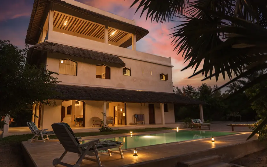 Modern villa with illuminated pool at dusk overlooking tropical gardens, Chuchungi House, Lamu Archipelago, Kenya