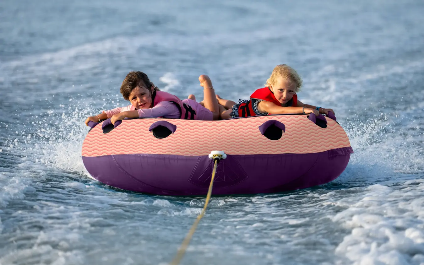 Two children riding in purple inflatable tube on ocean, Chuchungi House, Lamu Archipelago, Kenya