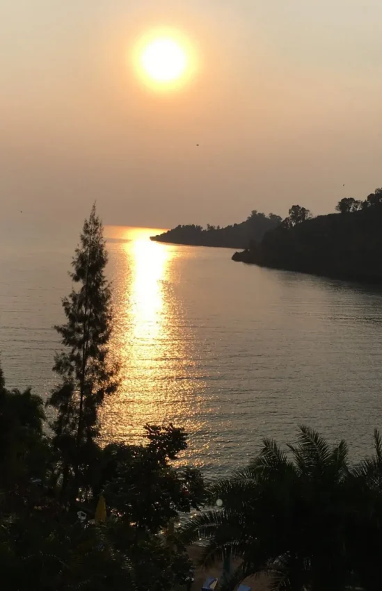 Golden sunset reflecting on calm river with forested shoreline and tropical vegetation, Cormoran Lodge, Lake Kivu, Rwanda