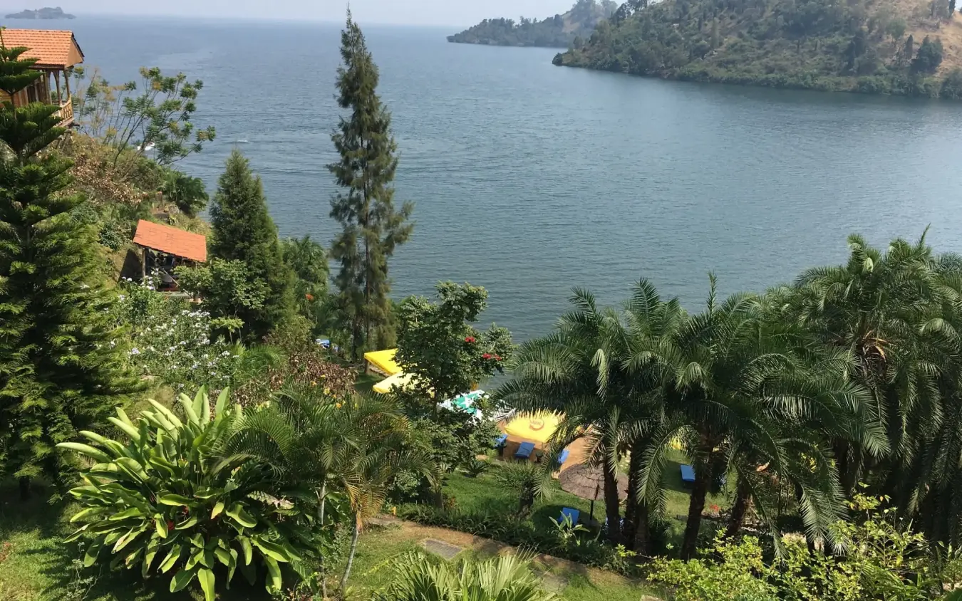 Lakeside resort with tropical gardens and moored boats on calm water, Cormoran Lodge, Lake Kivu, Rwanda