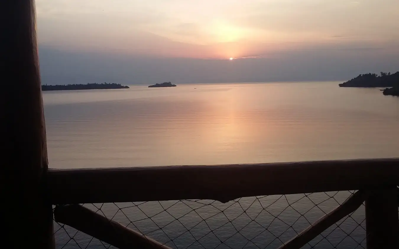 Sunset view over calm water from waterfront deck with islands silhouetted, Cormoran Lodge, Lake Kivu, Rwanda