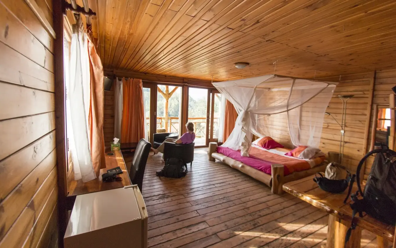 Spacious wooden lodge interior with canopy bed and valley views through large windows, Cormoran Lodge, Lake Kivu, Rwanda