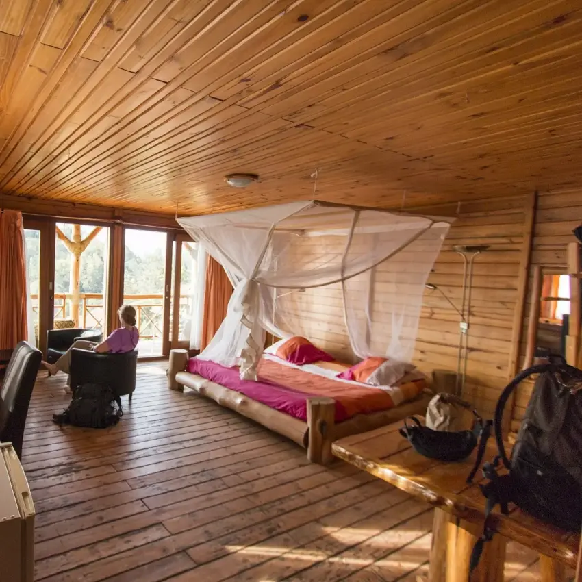 Spacious wooden lodge interior with canopy bed and valley views through large windows, Cormoran Lodge, Lake Kivu, Rwanda