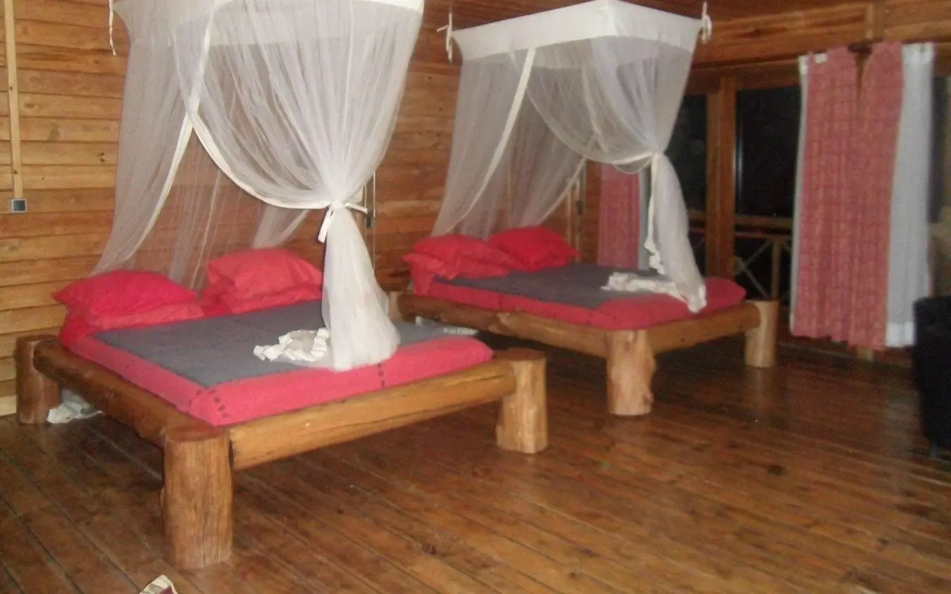 Luxury bedroom with four-poster beds and sheer canopies in wooden lodge, Cormoran Lodge, Lake Kivu, Rwanda