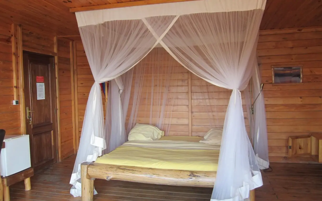 Four-poster bed with sheer drapes in wooden lodge bedroom, Cormoran Lodge, Lake Kivu, Rwanda