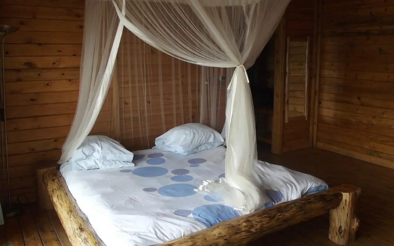Four-poster bed with sheer curtains in wooden lodge interior, Cormoran Lodge, Lake Kivu, Rwanda
