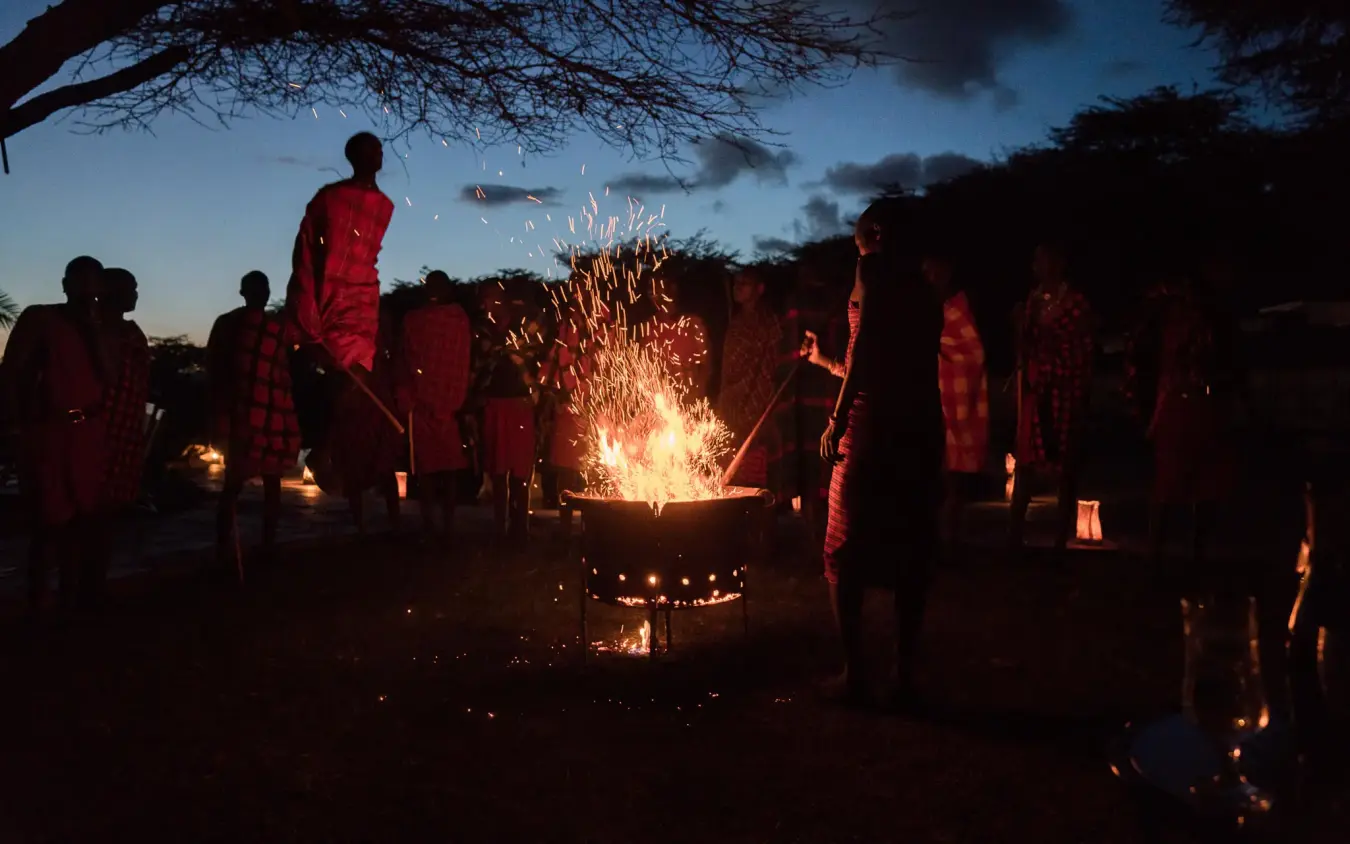 Guests gathered around evening fire under acacia tree, Cottar’s 1920s Camp, Maasai Mara, Kenya