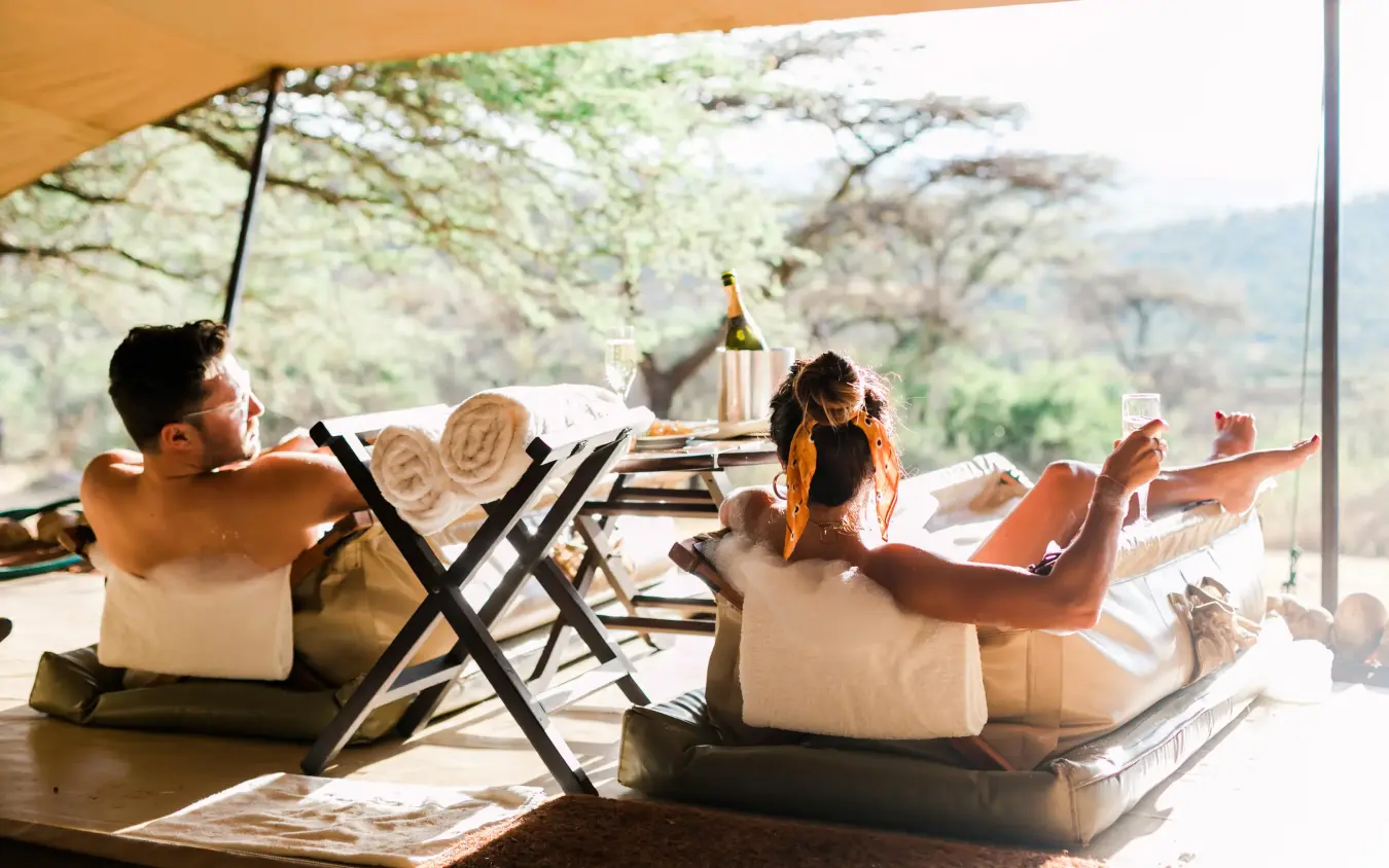 Guests relaxing on deck chairs under canvas canopy, Cottar’s 1920s Camp, Maasai Mara, Kenya