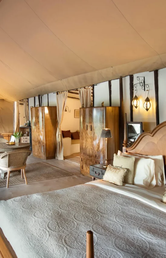Safari tent bedroom with wooden bed and cream furnishings, Cottar’s 1920s Camp, Maasai Mara, Kenya