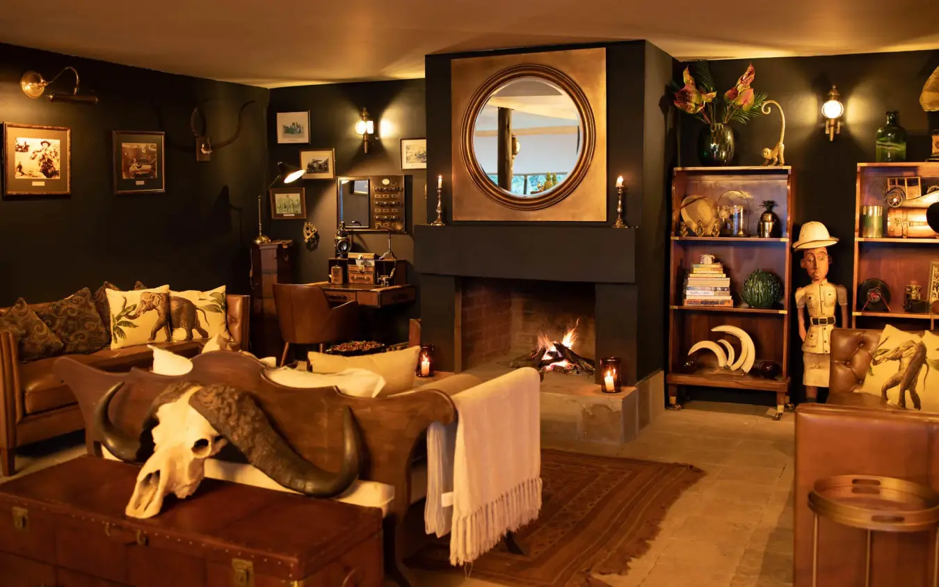 Safari lodge lounge with fireplace, vintage decor and round window, Cottar’s 1920s Camp, Maasai Mara, Kenya