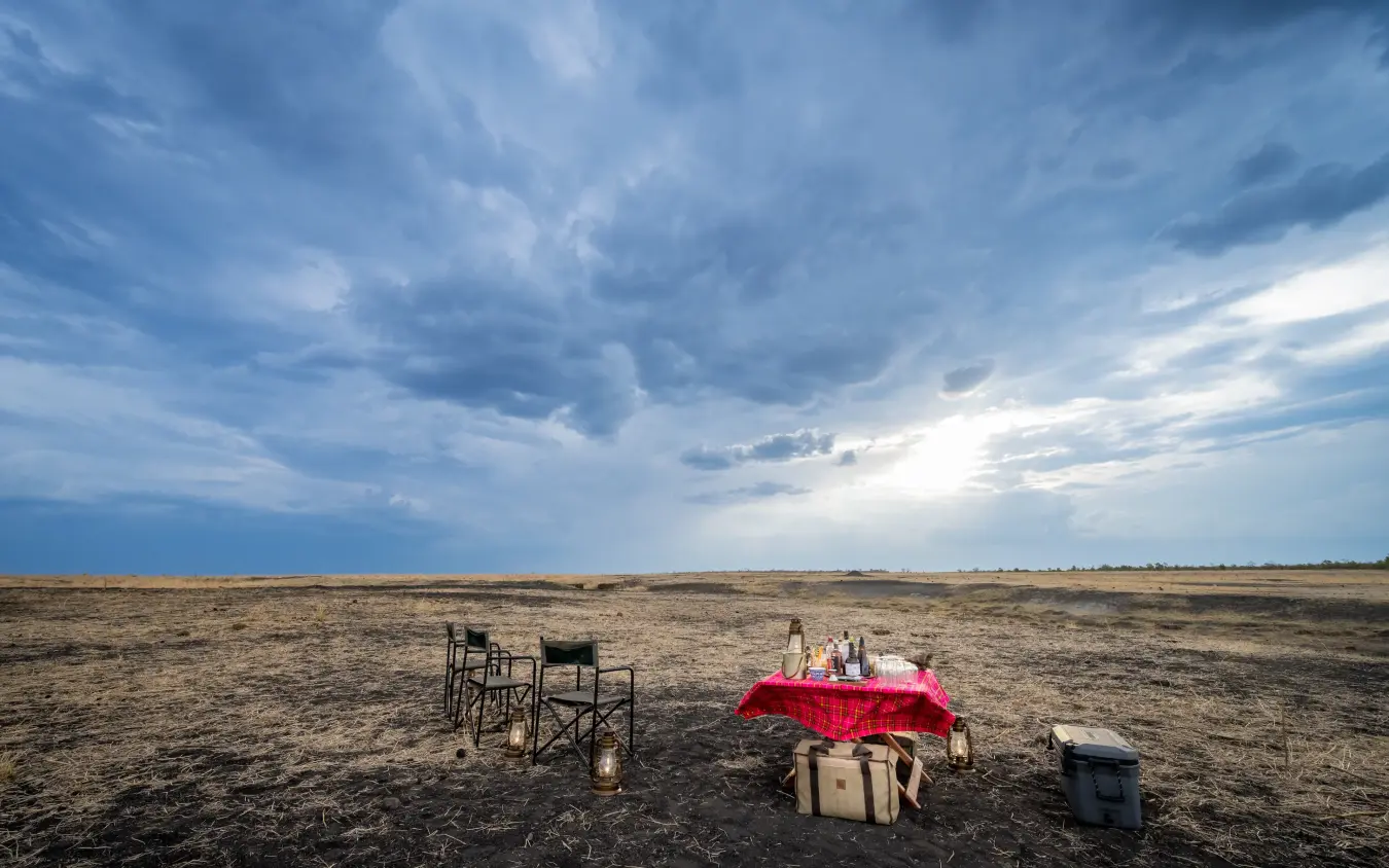 Dining setup with chairs and pink tablecloth on arid plain under dramatic sky, Daka Plains Camp, Hwange National Park, Zimbabwe