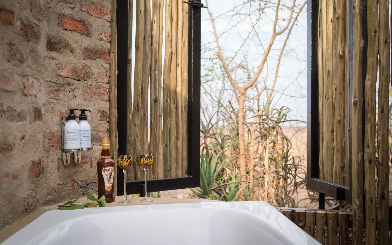 Freestanding bathtub with savanna views through wooden shutters, Daka Plains Camp, Hwange National Park, Zimbabwe