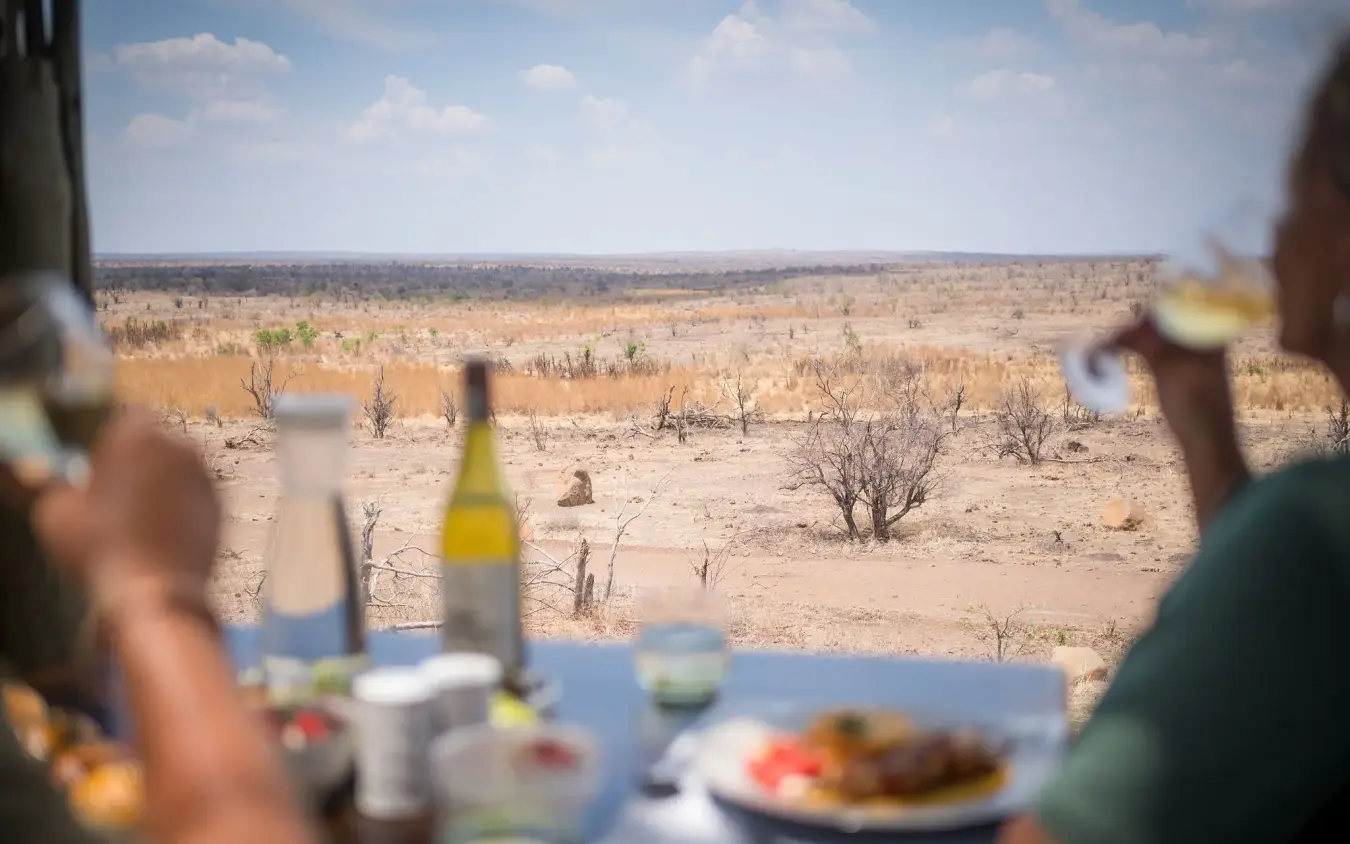 Outdoor dining with arid savanna landscape and sparse vegetation in background, Daka Plains Camp, Hwange National Park, Zimbabwe