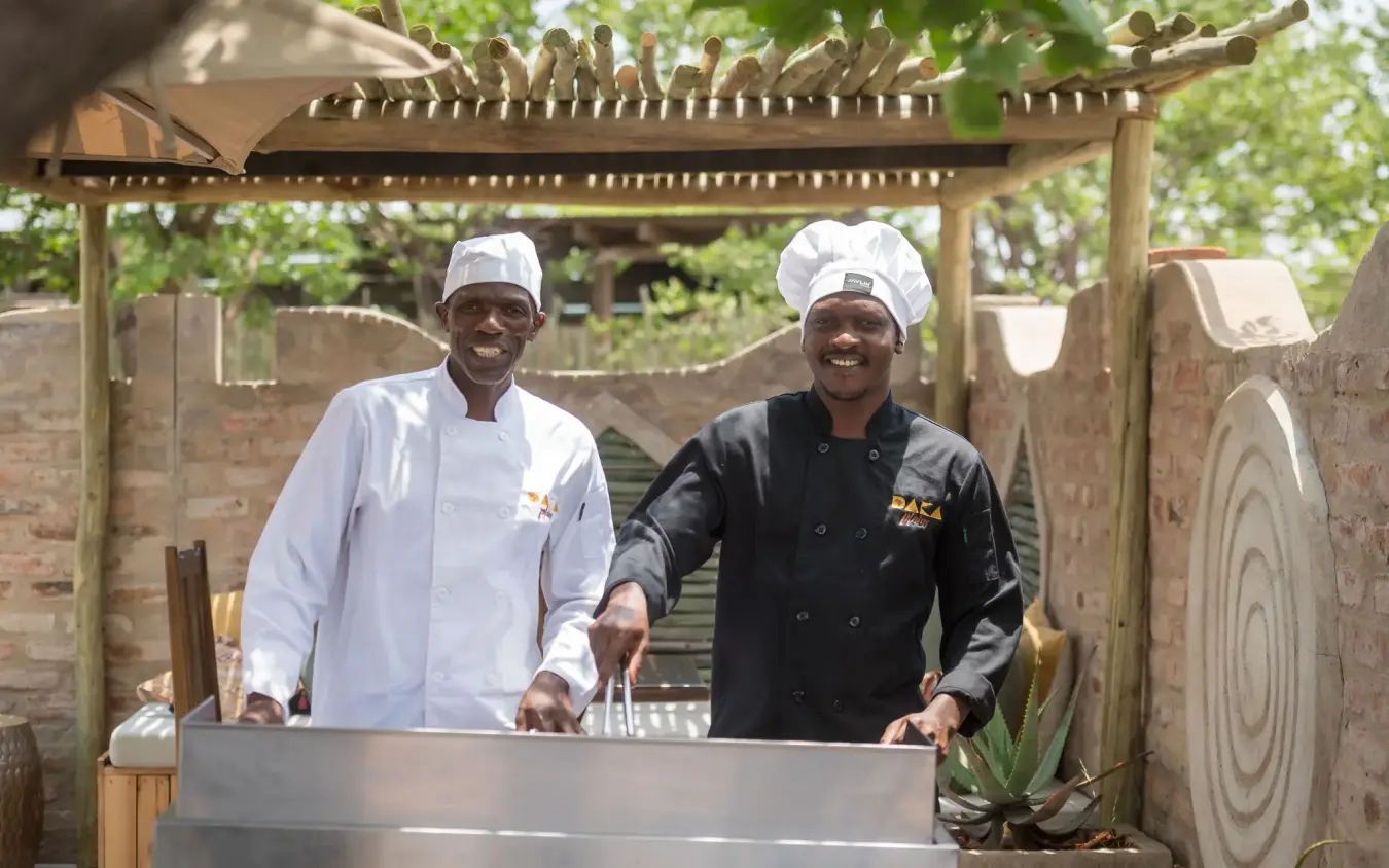 Two chefs in chef whites and black chef coats posing at outdoor cooking station, Daka Plains Camp, Hwange National Park, Zimbabwe