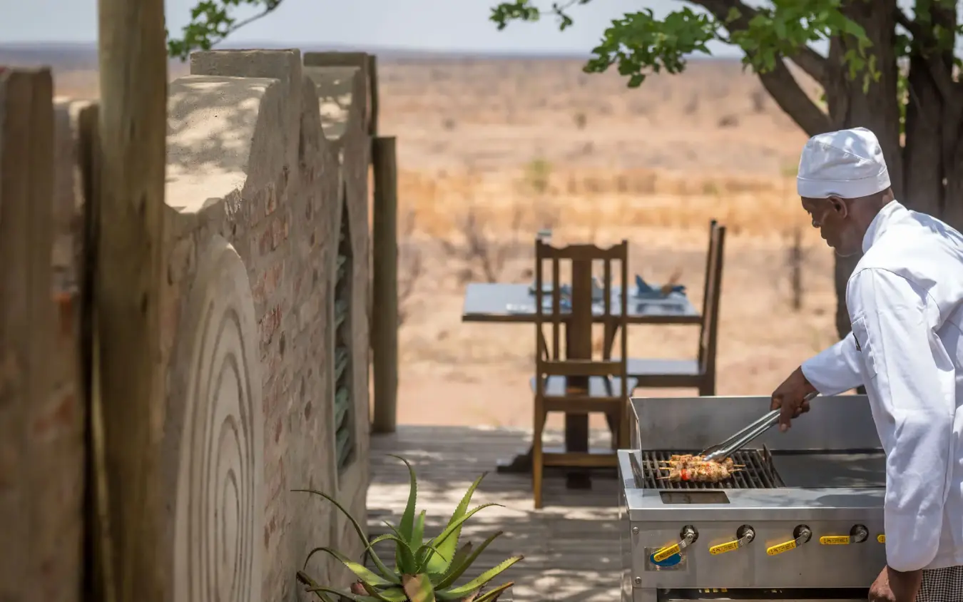 Chef grilling at outdoor kitchen overlooking vast savanna landscape, Daka Plains Camp, Hwange National Park, Zimbabwe