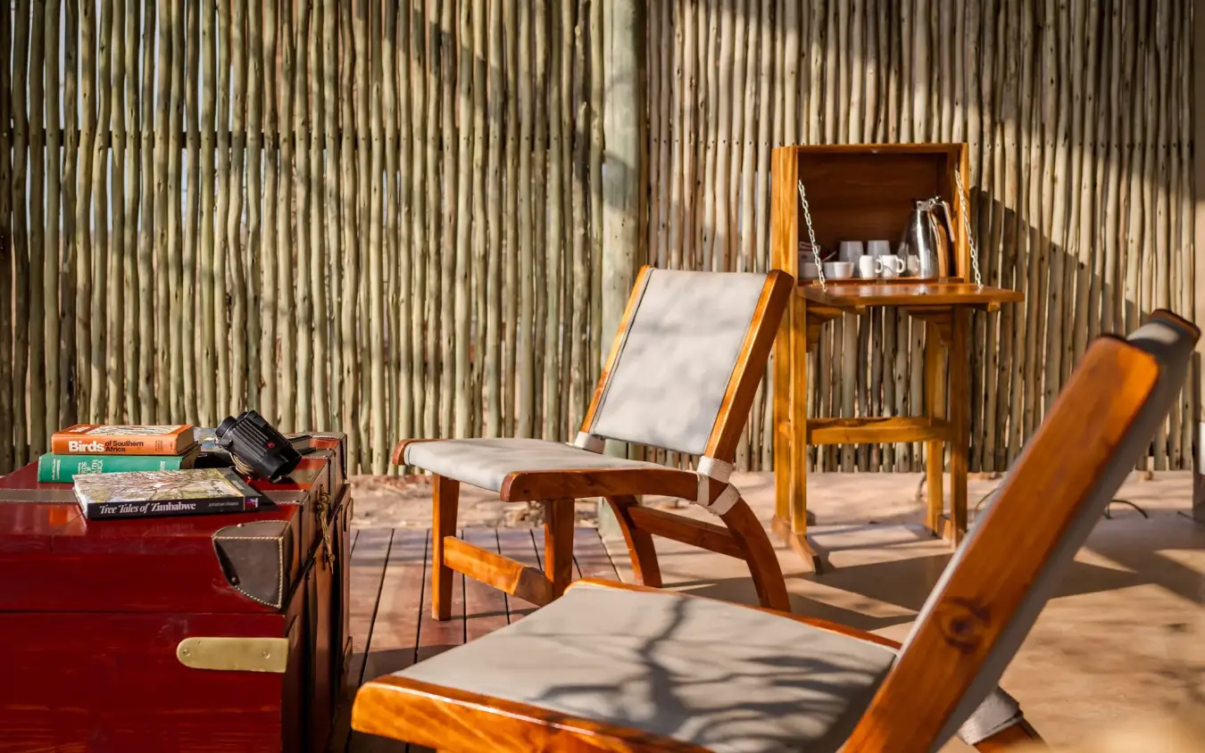Wooden deck chairs and side table on sandy terrace with corrugated metal wall, Daka Plains Camp, Hwange National Park, Zimbabwe