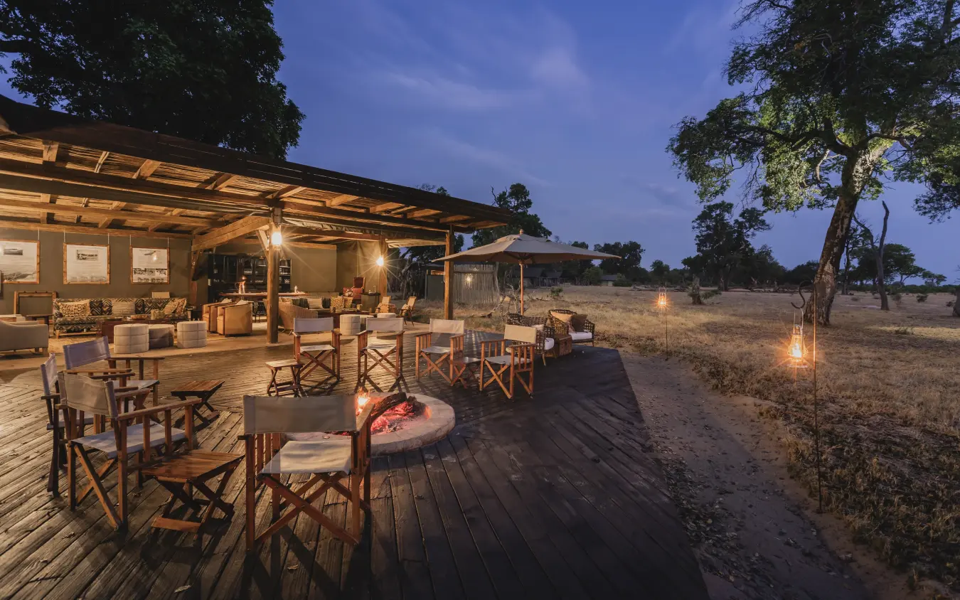 Outdoor lodge dining area with fire pit at dusk in savanna landscape, Davison’s Camp, Hwange National Park, Zimbabwe