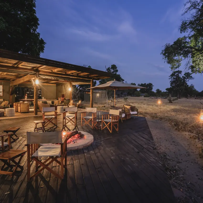 Outdoor lodge dining area with fire pit at dusk in savanna landscape, Davison’s Camp, Hwange National Park, Zimbabwe