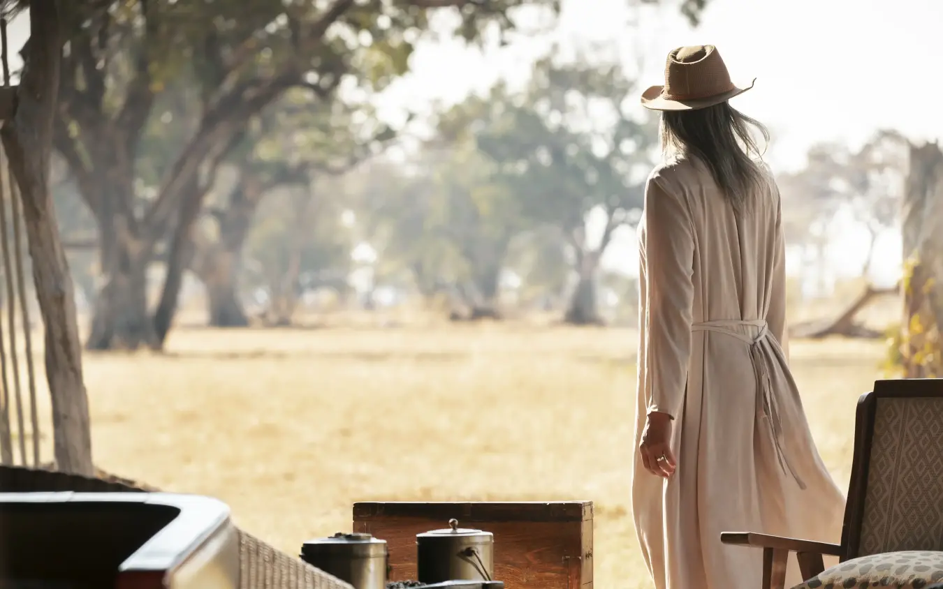 Woman in linen robe viewing savanna landscape from safari lodge veranda, Davison’s Camp, Hwange National Park, Zimbabwe