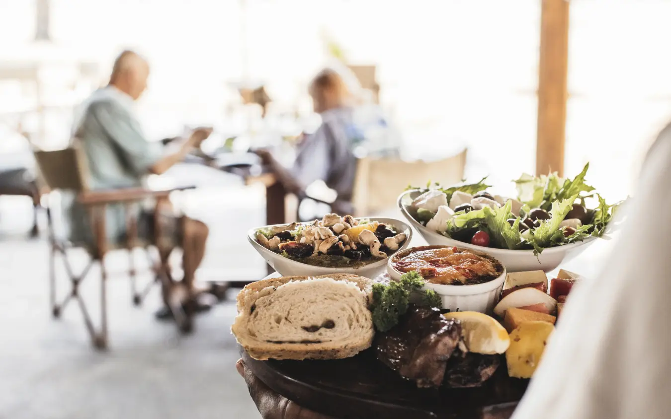 Outdoor dining table with fresh food and guests dining in background, Davison’s Camp, Hwange National Park, Zimbabwe