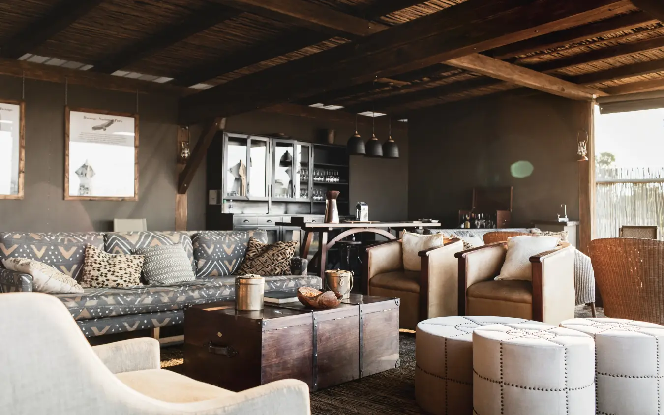 Luxury lounge interior with earth-toned furnishings and wooden beam ceiling, Davison’s Camp, Hwange National Park, Zimbabwe