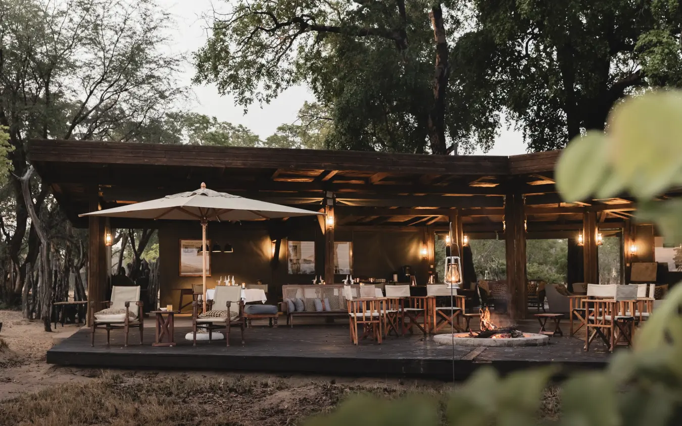 Luxury safari lodge with illuminated wooden structure nestled among acacia trees, Davison’s Camp, Hwange National Park, Zimbabwe