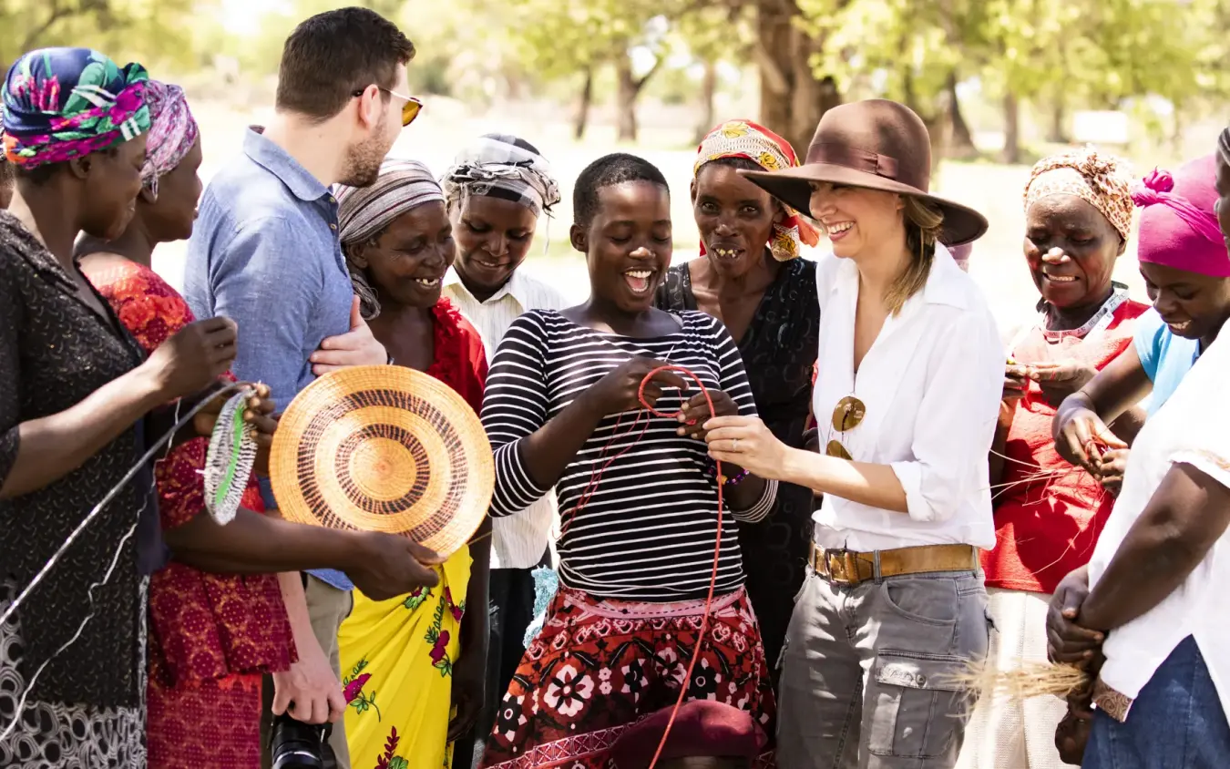 Group of visitors exchanging handmade crafts with local community members in park setting, Davison’s Camp, Hwange National Park, Zimbabwe