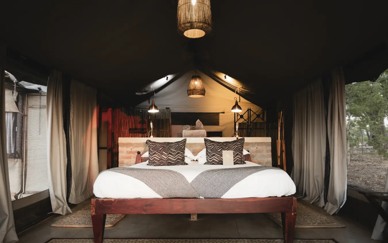 Luxury safari tent interior with king bed and ambient lighting at night, Davison’s Camp, Hwange National Park, Zimbabwe