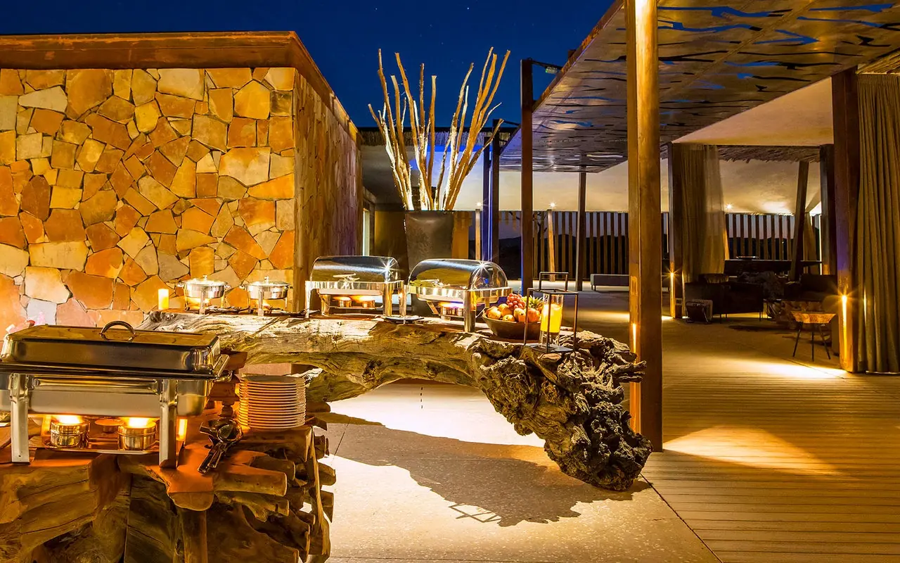 Illuminated outdoor terrace with stone wall and wooden deck at dusk, Dead Valley Lodge, Sossusvlei, Namibia